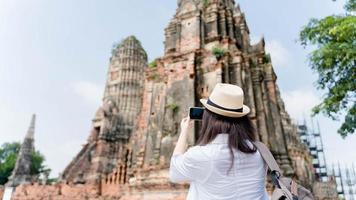 ung asiatisk kvinna tar Foto på hans mobil telefon kamera av en skön landskap medan stående nära tempel