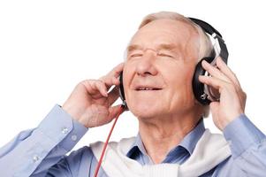 lyssnande till hans favorit musik. porträtt av glad senior man i hörlurar lyssnande till musik och förvaring ögon stängd medan stående mot vit bakgrund foto