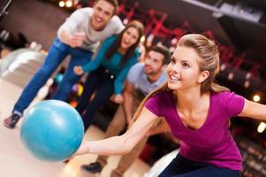 hon förälskelser detta spel. skön ung kvinnor kasta en bowling boll medan tre människor glädjande foto