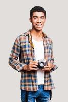 ung och kreativ. stilig ung Afroamerikan man innehav kamera och leende medan stående mot grå bakgrund foto