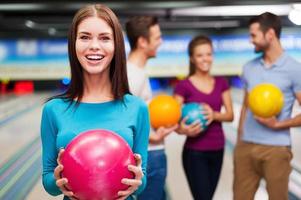 Vad kan vara bättre än bowling skön ung kvinnor innehav en bowling boll medan tre människor kommunicerar mot bowling gränder foto