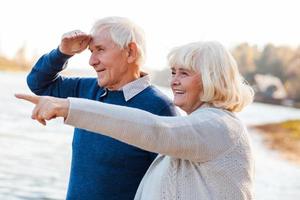 se över där Lycklig senior par stående på de kajkant tillsammans medan kvinna pekande bort och leende foto