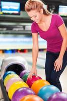 jag välja min favorit Färg. glad ung kvinnor välja bowling boll och leende medan stående mot bowling gränder foto