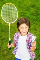 spela badminton topp se av Lycklig liten pojke innehav badminton racket och fjäderboll medan stående på grön gräs foto