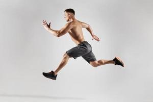 självsäker muskulös man med perfekt kropp löpning mot vit bakgrund foto