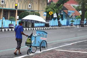 magelang, Indonesien, 2022 - Foto av en reser handlare tryckande en vagn på de sida av de väg i de eftermiddag