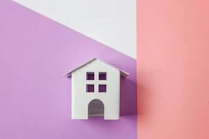 helt enkelt design med miniatyr- vit leksak hus isolerat på vit violett rosa pastell färgrik trendig geometrisk bakgrund. inteckning fast egendom försäkring dröm Hem begrepp. platt lägga topp se kopia Plats. foto