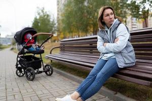 upprörd mor sitter på en bänk separerat från de pråm med henne bebis, de begrepp av postpartum depression foto