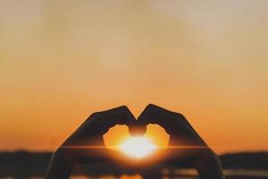 silhuett kärlek symbol hjärta symbol hand i de kväll solnedgång. foto