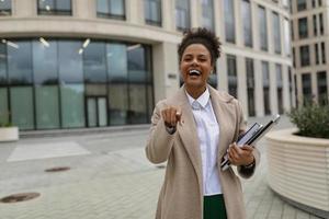 nöjd kvinna affärsman afrikansk amerikan kvinna med glad känslor poäng henne finger framåt- med en bred leende, framgångsrik företag handla begrepp foto