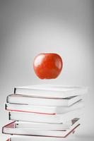 en röd äpple hänger ovan de böcker på en vit bakgrund. foto