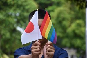 regnbåge flagga och japan nationell flagga innehav i hand, mjuk och selektiv fokus, begrepp för firande av lgbtq i stolthet månad runt om de värld. foto