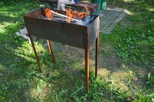 stor järn gjutjärn metall brasa för grill utegrill picknick kebab med trä- brinnande loggar i en bål med tungor av brand och rök foto