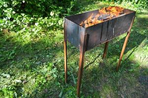 stor järn gjutjärn metall brasa för grill utegrill picknick kebab med trä- brinnande loggar i en bål med tungor av brand och rök foto