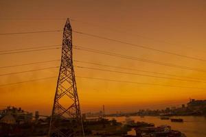 hög Spänning elektrisk pyloner med färgrik landskap efter solnedgång foto