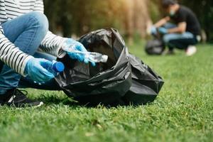 kvinnas hand plockar upp plast avfall för rengöring in i återvinna väska för rengöringat de parkera. clearing, förorening, ekologi och plast begrepp. foto