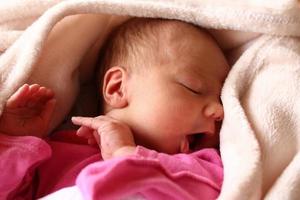 söt nyfödd bebis i rosa baud med ett öppen mun på henne säng under beige filt. foto