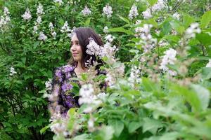 porträtt av skön ung kvinna i svart-lila klänning i en trädgård med blomning lila buskar. foto