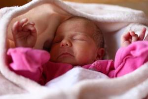 söt nyfödd bebis i rosa baud är sovande på henne säng under beige filt. foto