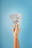 en hand med ett hundra dollar räkningar på en blå bakgrund. foto