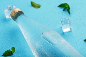 kall vatten flaska, is kuber, droppar och mynta löv på en blå bakgrund. foto