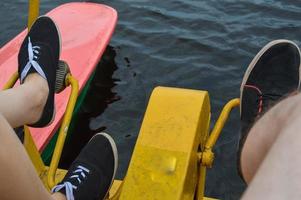 en flicka, en kvinna och en man vrida deras fötter på de trampa av en katamaran simning sport anläggning för avkopplande promenader på de sjö flod, hav vatten foto