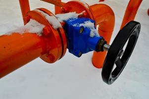 industriell stänga av reglerande skyddande rör beslag. svart ventil för öppning, stängning på ett järn orange metall rör med flänsar, dubbar, nötter mot de bakgrund av vit snö i vinter- foto