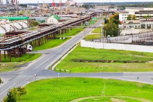 industriell landskap. panorama- se av de teknologisk rör. växt inställningar. från de kemisk röd vit rör rök är kommande. produktion byggnader. mot bakgrund av himmel och ljus gräs foto