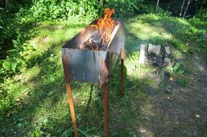 stor järn gjutjärn metall brasa för grill utegrill picknick kebab med trä- brinnande loggar i en bål med tungor av brand och rök foto