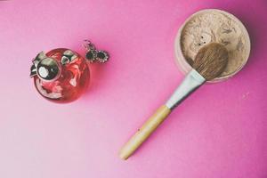 skönhet låda, smulig matt mineral pulver med en särskild naturlig brun trä- borsta från naturlig tupplur för smink, rosa parfym och skinande silver- örhängen på en rosa lila bakgrund. platt lägga. topp se foto