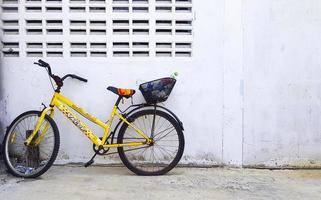 Bangkok, thailand-december 25, 2020 gammal gul cykel parkerad mot betong vägg med plast flaska eller avfall dumpning på svart korg i tillbaka och platt däck med kopia Plats. årgång eller bruten cykel. foto