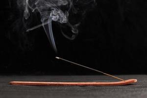 rök lockar av brinnande rökelse pinne i trä hållare för avkoppling och meditation svart bakgrund foto