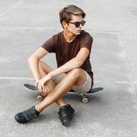 ung eleganta man i solglasögon Sammanträde på en skateboard. foto