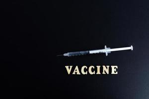 ett spruta med en dos av medicin eller vaccin på en svart bakgrund med en Plats för de text vaccinationer mot de influensa coronavirus foto