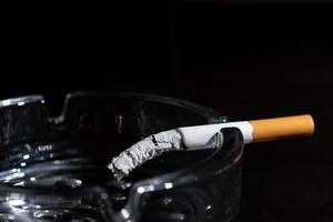 askkopp och rökning cigarett på svart bakgrund foto