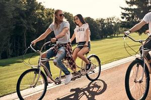 bra dag med vänner. grupp av Lycklig ung människor i tillfällig ha på sig leende medan cykling tillsammans utomhus foto