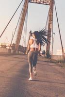på de flytta. full längd bak- se av skön ung kvinna i sporter Kläder löpning längs de bro foto