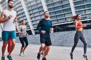 grupp av ung människor i sporter Kläder joggning medan utövar på de trottoar utomhus foto