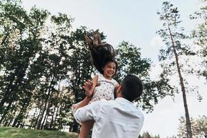 pappa är henne bäst vän. ung kärleksfull far bärande hans leende dotter medan utgifterna fri tid utomhus foto