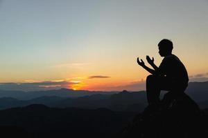 silhuett av en ung man bön- till Gud på de berg på solnedgång bakgrund. kvinna höjning hans händer i dyrkan. kristen religion begrepp. foto