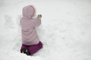 barn leker i snö. flicka på vintern. varma kläder på barnet. foto