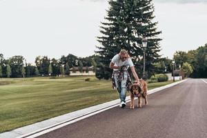tid för en promenad. full längd av stilig ung man gående med hans hund medan utgifterna tid utomhus foto