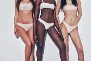 naturligtvis passa och skön. stänga upp av tre attraktiv blandad lopp kvinnor i underkläder stående mot grå bakgrund foto