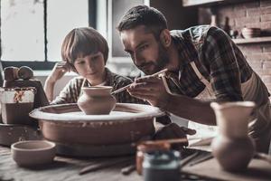 inlärning ny skicklighet. liten pojke ser på självsäker ung man teckning på keramisk pott på de krukmakeri klass foto