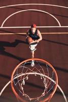 alltid riktade till vinna. topp se av ung man i sporter Kläder framställning till Göra en slam dunka medan spelar basketboll utomhus foto