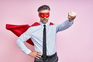 självsäker mogna man bär superhjälte cape och förvaring ärm utsträckt mot rosa bakgrund foto