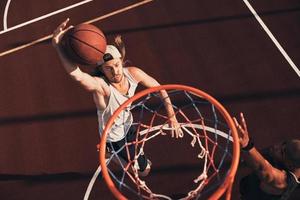 tryckande hård till vinna. topp se av ung man i sporter Kläder scoring en slam dunka medan spelar basketboll med vänner utomhus foto