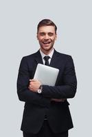 ung företag professionell. stilig ung man bärande digital läsplatta och leende medan stående mot grå bakgrund foto