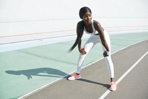 full längd av skön ung afrikansk kvinna i sporter Kläder avkopplande efter Träning medan stående utomhus foto