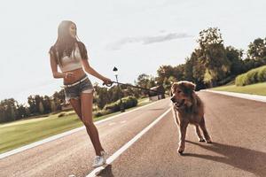 ser för äventyr tillsammans. full längd av skön ung kvinna spelar med henne hund och leende medan löpning utomhus foto